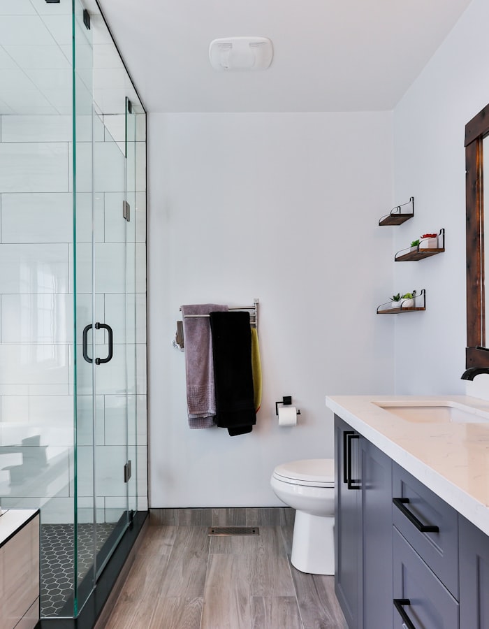 Un baño reformado con ducha de cristal, lavabo moderno, inodoro blanco y estanterías de pared.
