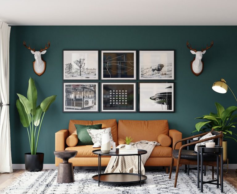 Salón con pared verde oscuro, sofá mostaza, cuadros enmarcados, plantas altas y decoración de estilo moderno.