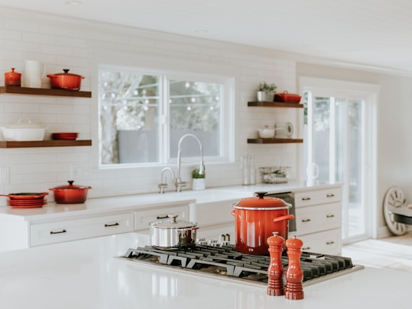 Una cocina blanca y luminosa muestra ollas y utensilios rojos sobre una isla central con fogones.